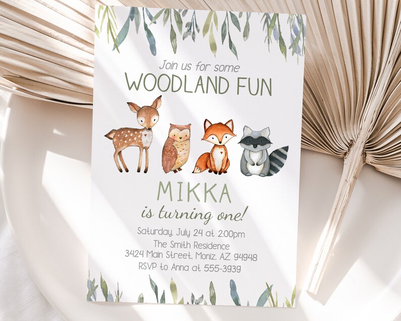 May include: A white invitation card with watercolor illustrations of woodland animals: a deer, owl, fox, and raccoon. The text reads "Join us for some WOODLAND FUN" and "MIKKA is turning one!" with event details.