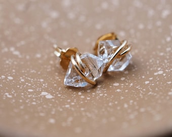 May include: A pair of gold earrings with clear crystal stones. The stones are wrapped in gold wire and have a geometric shape.