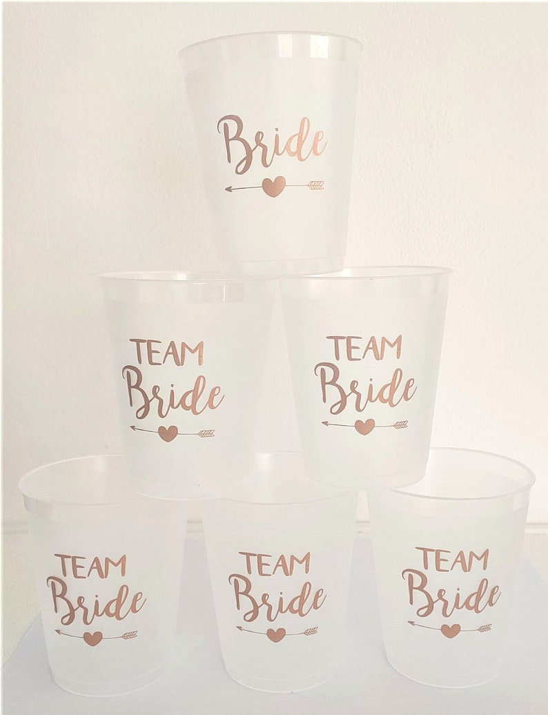 May include: Set of six clear plastic cups with gold lettering. The cups have the words "Bride" and "Team Bride" printed on them.