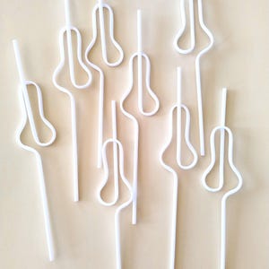 May include: A collection of white plastic drinking straws bent into various shapes. The straws are arranged in a vertical pattern on a light brown background.