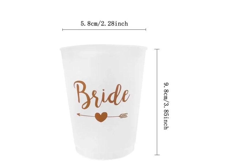 May include: White plastic cup with the word "Bride" in gold lettering and a gold arrow with a heart. The cup is 5.8 cm wide and 9.8 cm tall.