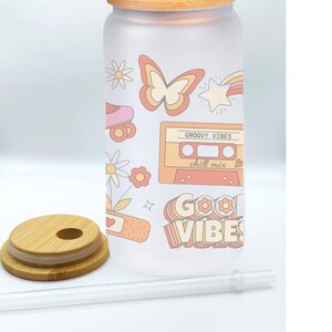 May include: A frosted glass water bottle with a bamboo lid and straw. The bottle has a retro design with a butterfly, roller skates, a cassette tape, and the text "Groovy Vibes chill mix" and "Good Vibes".