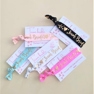 May include: A set of six hair ties with gold glitter and the text "Team Bride" in gold lettering. The hair ties are on cards with the text "The best 'I do' crew you've ever seen."