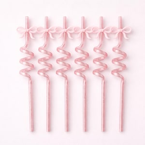 Peut inclure: Six pailles décoratives roses avec un motif en spirale et un petit nœud en haut. Les pailles sont disposées verticalement sur un fond rose uni, créant une esthétique douce et élégante.
