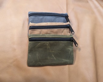 May include: Three rectangular zippered pouches stacked vertically. The top pouch is charcoal gray, the middle is tan, and the bottom is olive green. Each pouch features a black zipper closure along the top edge with a matching black metal pull tab.