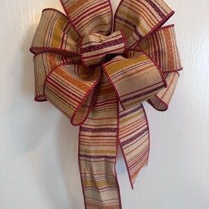 May include: A large, striped bow made from a beige fabric with red, orange, and brown stripes. The bow is tied with a long tail.