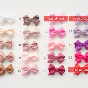 May include: A collection of satin hair bows in various colors, including white, beige, pink, and purple. Some bows are marked as "sold out". These bows are suitable for various occasions and styles.