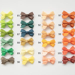 May include: A collection of small, colorful bows in various shades, including yellow, green, blue, and orange. Each bow is labeled with a number from 79 to 102. These bows are likely used for crafting or hair accessories.