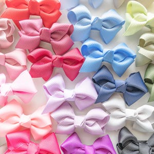 May include: A collection of colorful grosgrain ribbon hair bows in various shades of pink, red, blue, green, and purple. The bows are arranged closely together, creating a vibrant and textured display. These bows are suitable for all ages.