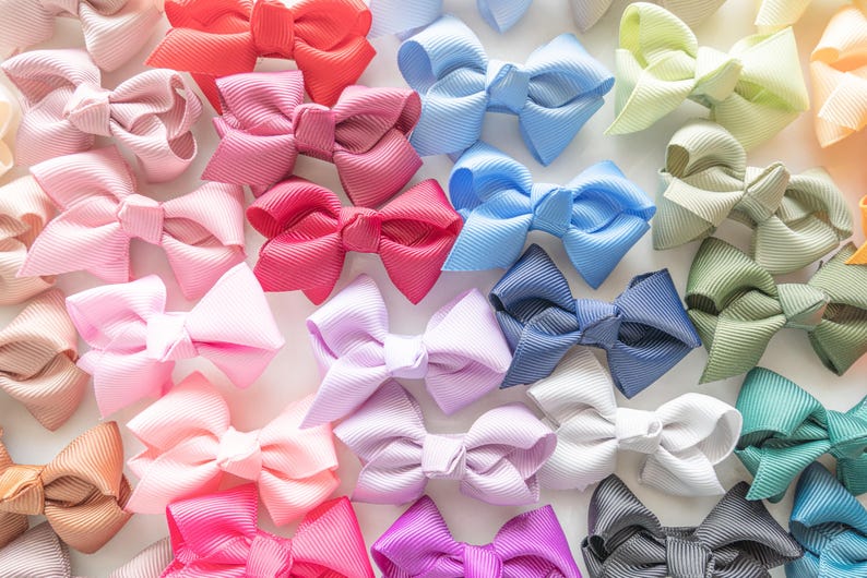 May include: A collection of colorful grosgrain ribbon hair bows in various shades of pink, red, blue, green, and purple. The bows are arranged closely together, creating a vibrant and textured display. These bows are suitable for all ages.