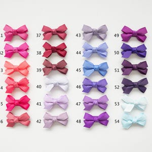 May include: A collection of 24 small, colorful bows arranged in rows. The bows range in color from pinks and reds to purples and blues, with each bow labeled with a number from 31 to 54. The bows are made of a textured fabric.