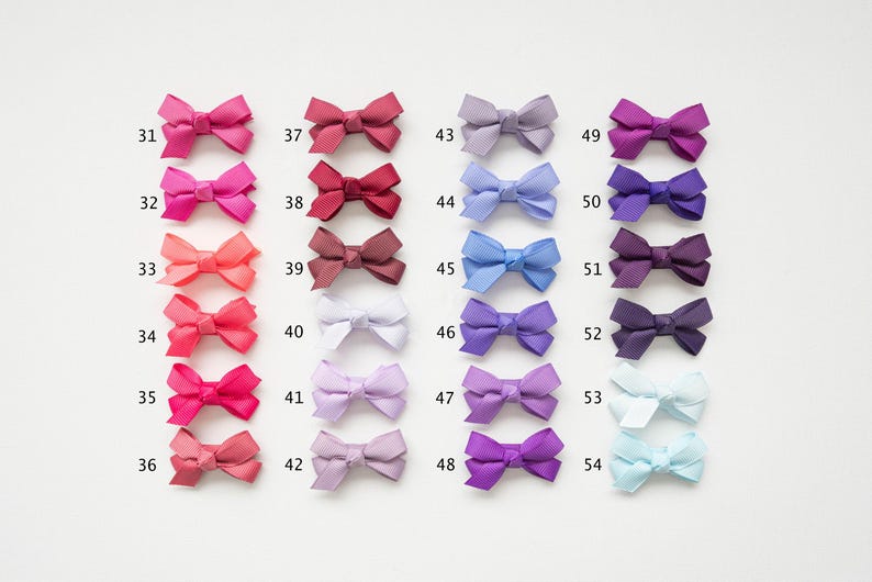 May include: A collection of 24 small, colorful bows arranged in rows. The bows range in color from pinks and reds to purples and blues, with each bow labeled with a number from 31 to 54. The bows are made of a textured fabric.