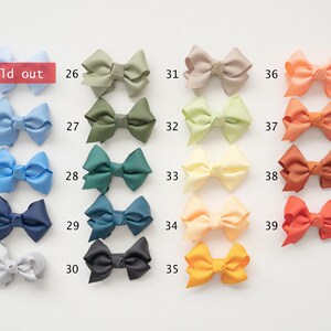 May include: A collection of colorful hair bows in various shades, including blue, green, yellow, and orange. Each bow is neatly arranged and numbered, with one labeled "sold out". The bows are made of a smooth, possibly satin-like material.