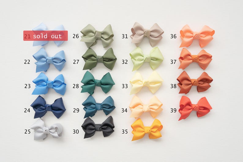 May include: A collection of colorful hair bows in various shades, including blue, green, yellow, and orange. Each bow is neatly arranged and numbered, with one labeled "sold out". The bows are made of a smooth, possibly satin-like material.