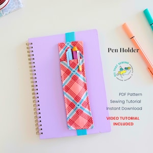 May include: A lavender spiral-bound notebook with a coral, blue, and white plaid fabric pen holder attached by a turquoise elastic band. The pen holder contains two pens. Text reads: Pen Holder, ALL THAT SEWING, PDF Pattern Sewing Tutorial, Instant Download, VIDEO TUTORIAL INCLUDED.