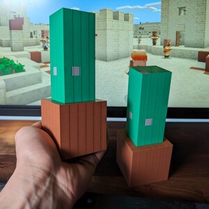 Könnte beinhalten: Zwei grüne und braune Minecraft-Kaktusblöcke. Die Blöcke sind aus Kunststoff und etwa 10 cm hoch.