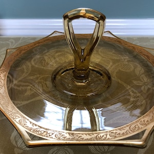 May include: A gold-rimmed glass serving tray with a gold-colored handle. The tray has a scalloped edge and a floral design.