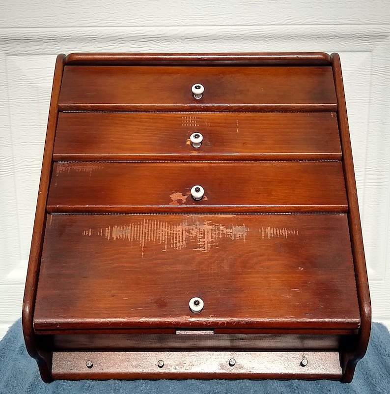 Puede incluir: Una panera de madera vintage con cuatro cajones y pomos de porcelana blanca. La panera tiene un acabado desgastado y est&aacute; hecha de madera maciza.