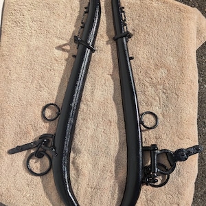 May include: A pair of black metal horse collar hames with brass accents. The hames are connected by a chain.