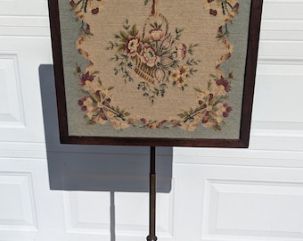 Può includere: Un parascintille in legno vintage con un design a punto ago floreale. Lo schermo è su un supporto a treppiede con un puntale tornito.