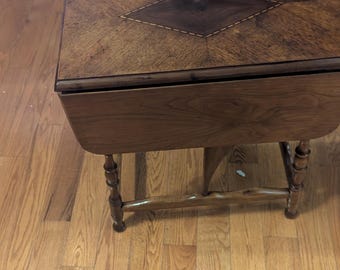 ¡Hallazgo excepcional! Preciosa mesa auxiliar plegable de estilo colonial en nogal, con increíbles incrustaciones de madera de parqué y patas torneadas a mano.