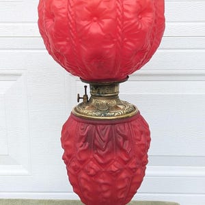 May include: A vintage red glass lamp with a round shade and a decorative base. The lamp features a textured pattern on the shade and a brass-colored metal base. The lamp is a decorative lighting fixture.