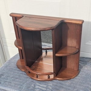 May include: A dark brown wooden wall shelf with a curved top and bottom. It features two small shelves on the sides and a mirrored back. The shelf has a classic, vintage design.
