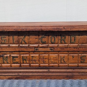 May include: A vintage wooden sewing box with two drawers. The top drawer reads "SIX CORD" and the bottom drawer reads "MERRICK'S" in carved lettering. The box has round wooden knobs and a dark brown finish.