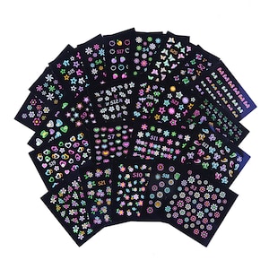 Könnte beinhalten: Eine Sammlung schwarzer Nagelkunst-Aufkleberbögen mit verschiedenen Designs. Die Aufkleber zeigen Blumen, Sterne, Herzen, Schmetterlinge und andere Formen in leuchtenden Neonfarben. Jedes Blatt ist mit einer Nummer versehen.