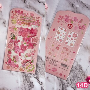Pu&ograve; includere: Due confezioni di adesivi di fiori di ciliegio rosa. Una confezione contiene singoli adesivi, l'altra fogli di adesivi con disegni floreali. Gli adesivi presentano fiori di ciliegio rosa e bianchi e foglie verdi.