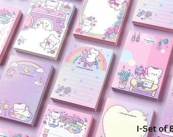 Puede incluir: Un conjunto de ocho blocs de notas con fondos en tonos pastel rosa, morado y blanco. Cada bloc presenta una ilustración de oso diferente con arcoíris, dulces y otros diseños caprichosos. El texto "mengmengbear" es visible en algunos blocs.