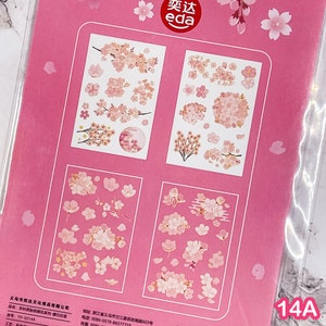 Pu&ograve; includere: Foglio di adesivi rosa con disegni di fiori di ciliegio. Gli adesivi mostrano singoli fiori, grappoli e rami in rosa e bianco. Il foglio include il testo "奕达 eda" e il numero "14A".