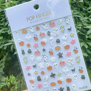 May include: A sheet of 3D nail stickers with Halloween designs. The stickers feature pumpkins, ghosts, stars, flowers, and black cats. The package is labelled "POP FINGER 3D Design Nail Sticker". The sticker sheet is in a clear plastic package.
