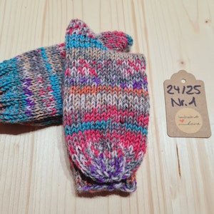 Könnte beinhalten: Ein Paar bunte handgestrickte Socken in den Farben Grau, Rosa, Orange, Blau und Lila. Die Socken sind mit einem braunen Etikett versehen, auf dem "24/25 Nr. 1 handmade with love" steht.