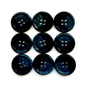 May include: Nine dark blue buttons with four holes each are arranged in a three-by-three grid. The buttons have a marbled appearance with subtle variations in color, creating a textured look. The buttons are round and sit against a white background.
