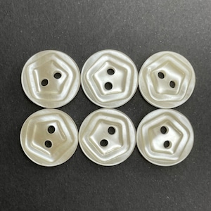 Puede incluir: Seis botones de plástico blanco con dos agujeros cada uno. Los botones tienen un diseño elevado de cinco lados.