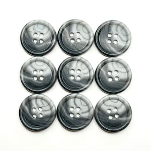 Puede incluir: Ocho botones grises con forma de espiral con cuatro agujeros cada uno. Los botones son de plástico y tienen un aspecto marmoleado.