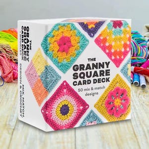 May include: A white box featuring colorful crochet granny square designs. The text "THE GRANNY SQUARE CARD DECK" is prominently displayed, along with "50 mix & match designs." The box also includes a booklet for design and crochet.