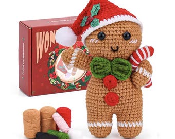 Könnte beinhalten: Eine gehäkelte Lebkuchenfigur mit einer rot-weißen Weihnachtsmütze mit grünem Stechpalmen-Akzent, einer grünen Fliege und zwei roten Knöpfen. Die Figur hält eine rot-weiß gestreifte Zuckerstange. Eine rote Schachtel mit der Aufschrift WONDER und Garn.