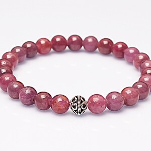 May include: A pink gemstone bracelet with a silver bead charm. The bracelet is made of round beads and has a simple design.