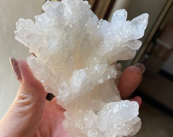 Op de afbeelding: Een cluster van witte, doorschijnende kristallen met een ruw, getextureerd oppervlak. De kristallen zijn in een cluster gerangschikt, die lijkt op een kleine boom of struik.