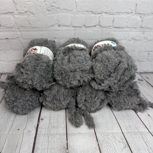 May include: Three skeins of grey fluffy yarn, each with a white label. The yarn is soft and fluffy, perfect for knitting or crocheting.