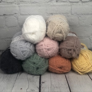 Peut inclure: Une collection de dix pelotes de laine de différentes couleurs, dont blanc, beige, rose, marron, vert, orange et jaune. La laine est douce et moelleuse, idéale pour le tricot ou le crochet.