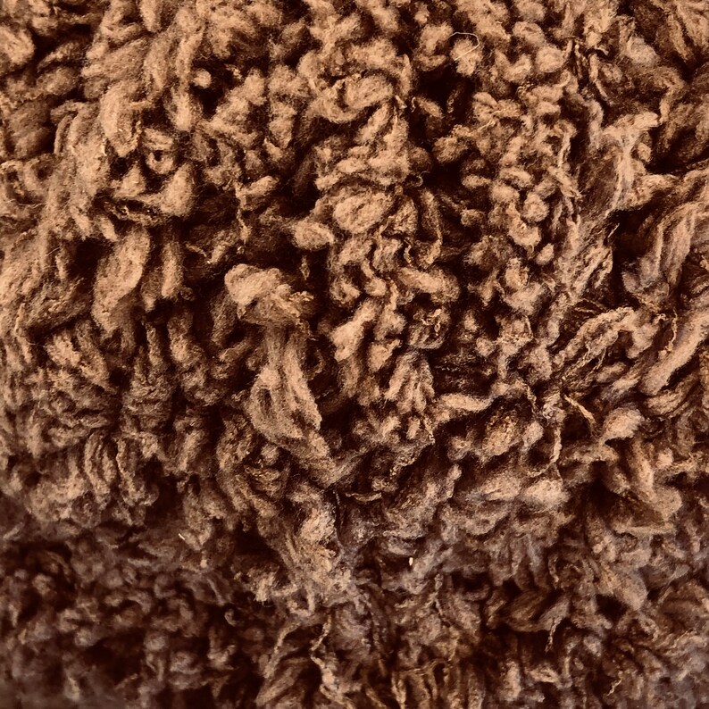 May include: Close-up of a brown, fluffy, textured fabric. The fabric has a soft, fuzzy appearance.