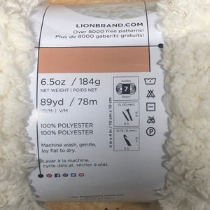 May include: A white yarn ball with a label that says "Lion Brand.com" and includes information about the yarn, such as the weight, length, fiber content, and care instructions. The label also includes a size guide for knitting needles and crochet hooks.