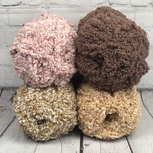 May include: Three balls of yarn in different colors: pink, brown, and beige. The yarn is fluffy and textured.