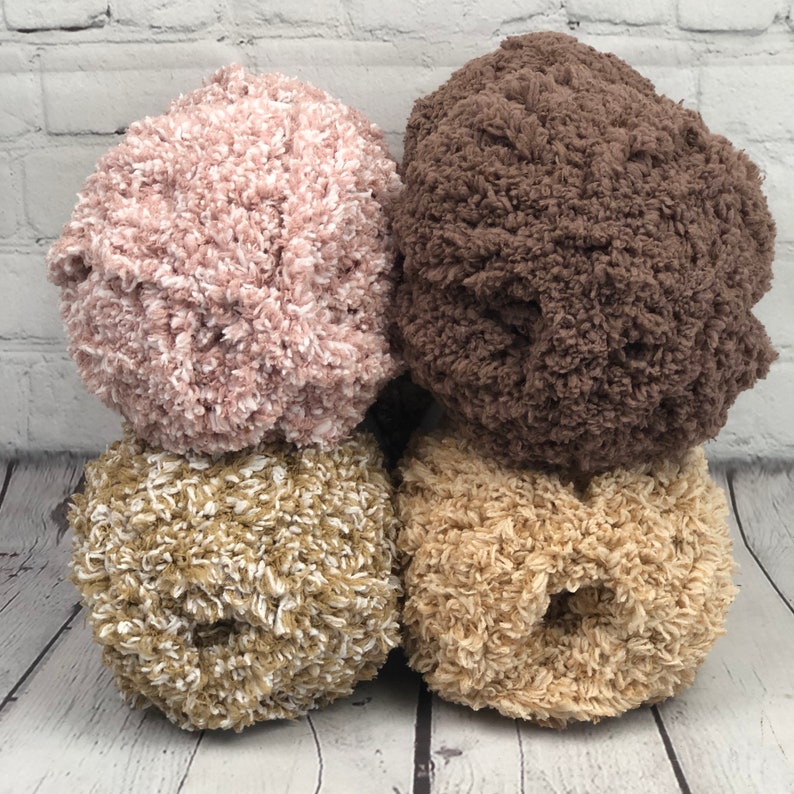 May include: Three balls of yarn in different colors: pink, brown, and beige. The yarn is fluffy and textured.