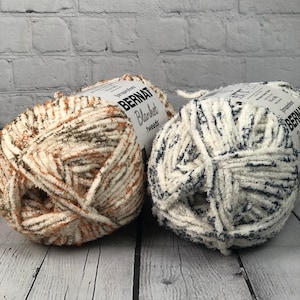 May include: Two skeins of Bernat Blanket yarn. One skein is a cream color with brown and green flecks. The other skein is a cream color with blue flecks.