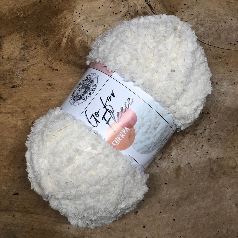 May include: A white skein of Go for Fleece Sherpa yarn. The yarn is soft and fluffy, and it is perfect for making blankets, scarves, and other cozy items.
