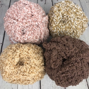 May include: Four balls of yarn in different colours: pink with white, beige with white, beige, and brown. The yarn is fluffy and textured.